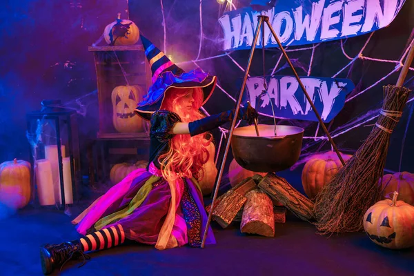 Kis gyönyörű lány boszorkány jelmezben ünnepli Boldog Halloween party belső tökkel — Stock Fotó
