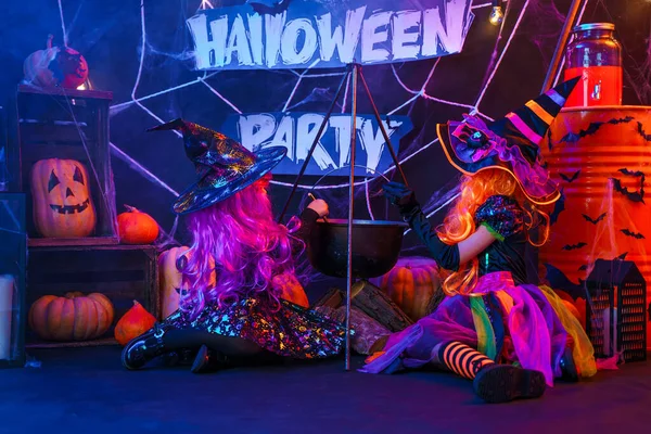Две маленькие красивые девочки в костюме ведьмы празднует счастливый Хэллоуин партии, заварив зелье в паровой чан, интерьер с тыквами — стоковое фото
