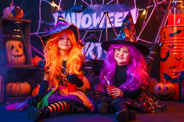 Dvě malé krásné dívky v kostýmech čarodějnice slaví Happy Halloween party v interiéru s dýněmi — Stock fotografie