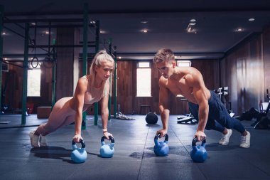 Genç çift spor salonunda çalışıyor. Çekici kadın ve yakışıklı kaslı adam modern spor salonunda eğitim görüyor. Kettlebell 'de kalas yapıyorum. Ağırlıklarda şınav