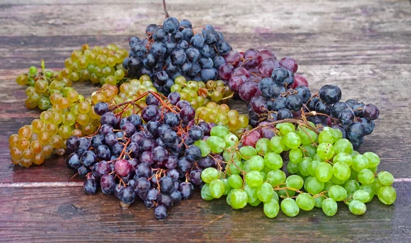 Red, black and white (green) grapes on a wooden table