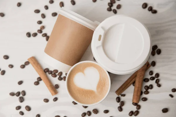 Coffee and coffee paper cups on a light background with cinnamon sticks and coffee beans