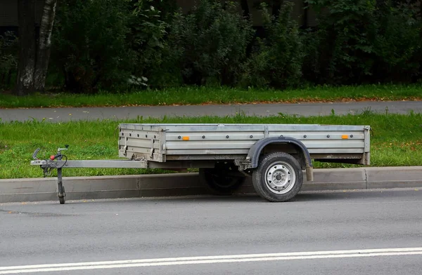 Yeşil bir çimenliğin yanındaki yolda açık bir otomobil römorku var.