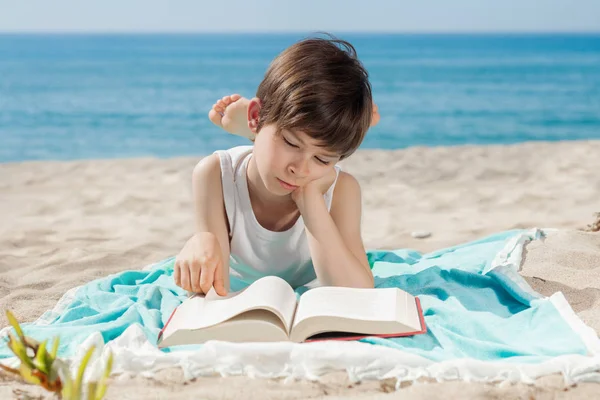 Menino com livro deitado na praia um dia ensolarado — Fotografia de Stock