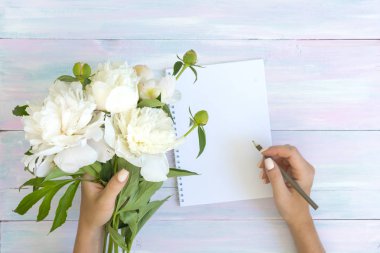 Eller bir defterde yazmak. Peonies ve bir ahşap zemin üzerinde. Doku. Sosyal ağlar için bir fotoğraf. Düz yatıyordu masaları