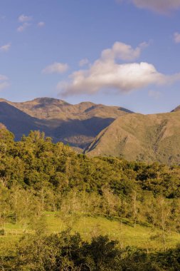 Günbatımının ışığıyla aydınlatılan görkemli Iguaque dağı yamacındaki ormanlarla ve çiftliklerle ve vadideki körükle.