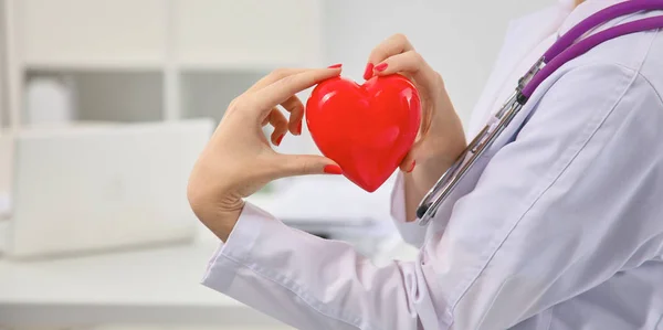 Młoda kobieta lekarz trzymając czerwonym sercem, w biurze — Zdjęcie stockowe