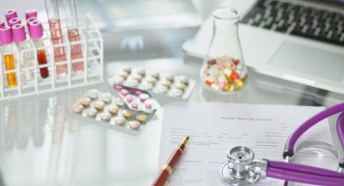 closeup of the desk of a doctors office with a stethoscope in the foreground and a bottle with pills in the background, selective focus clipart