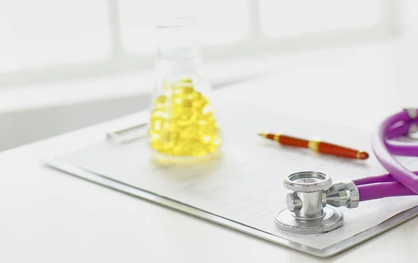 Close-up da mesa de um consultório médico com um estetoscópio em primeiro plano e uma garrafa com pílulas no fundo, foco seletivo — Fotografia de Stock