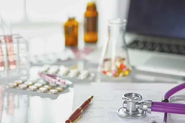 Close-up da mesa de um consultório médico com um estetoscópio em primeiro plano e uma garrafa com pílulas no fundo, foco seletivo — Fotografia de Stock