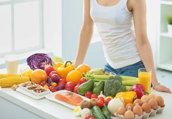 Jovem dona de casa feliz sentado na cozinha preparando alimentos de uma pilha de frutas e legumes orgânicos frescos diversos, foco seletivo — Fotografia de Stock