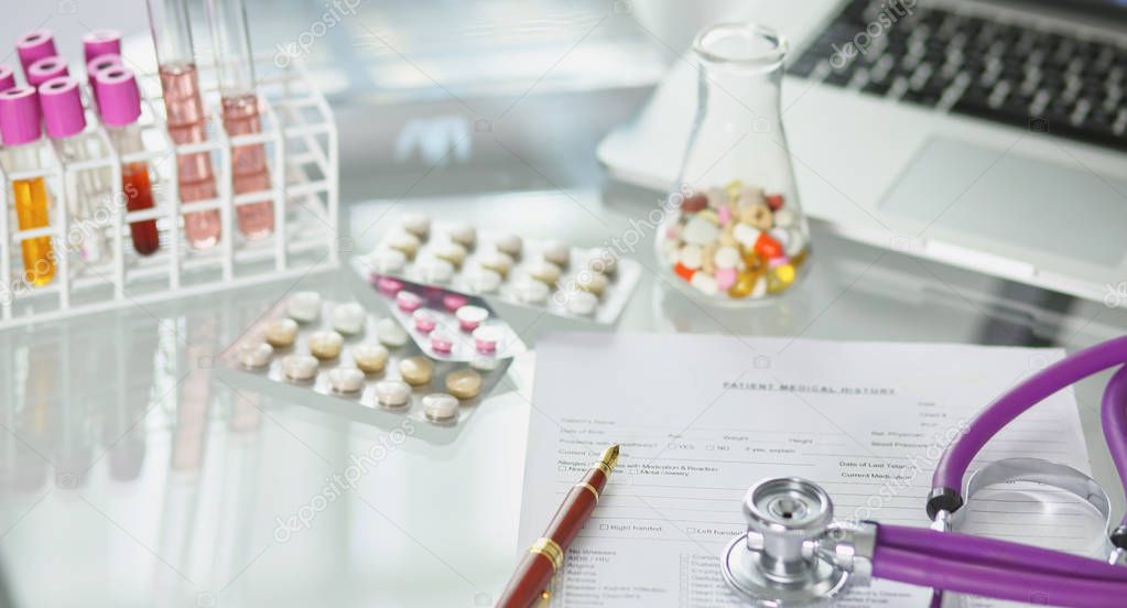 closeup of the desk of a doctors office with a stethoscope in the foreground and a bottle with pills in the background, selective focus