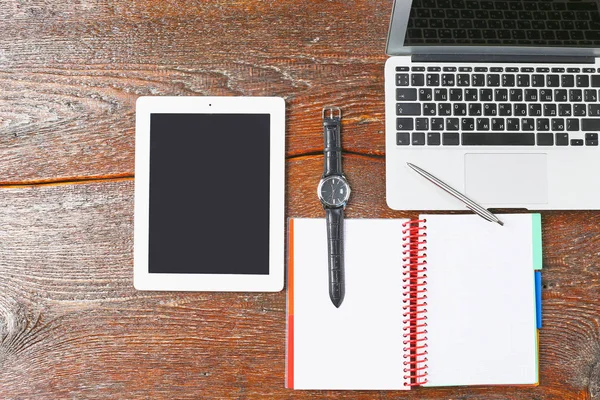 Dizüstü bilgisayar, tablet ve defter üzerinde ahşap bir masa vardır