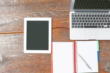 Dizüstü bilgisayar, tablet ve defter üzerinde ahşap bir masa vardır