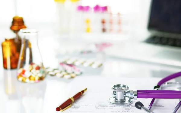 Closeup of the desk of a doctors office with a stethoscope in the foreground and a bottle with pills in the background, selective focus — Stock Photo, Image