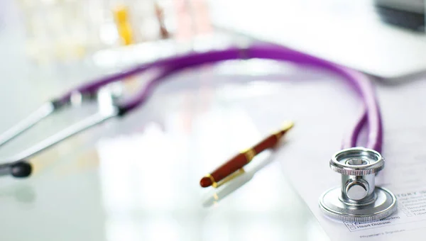 Closeup of the desk of a doctors office with a stethoscope in the foreground and a bottle with pills in the background, selective focus — Stock Photo, Image