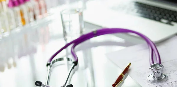 Closeup of the desk of a doctors office with a stethoscope in the foreground and a bottle with pills in the background, selective focus — Stock Photo, Image