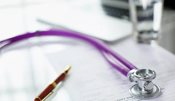 Closeup of the desk of a doctors office with a stethoscope in the foreground and a bottle with pills in the background, selective focus — Stock Photo, Image