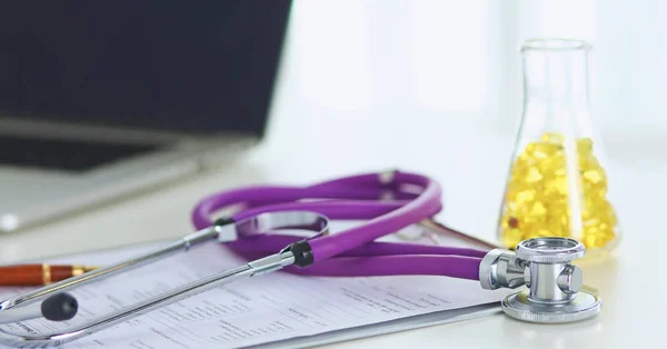 Close-up da mesa de um consultório médico com um estetoscópio em primeiro plano e uma garrafa com pílulas no fundo — Fotografia de Stock