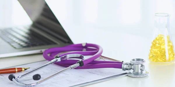 Primer plano del escritorio de un consultorio médico con un estetoscopio en primer plano y una botella con pastillas en el fondo — Foto de Stock