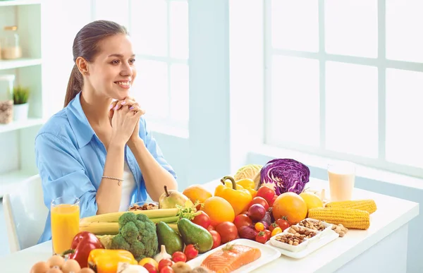 Щаслива молода домогосподарка сидить на кухні готує їжу з купи різноманітних свіжих органічних фруктів і овочів — стокове фото