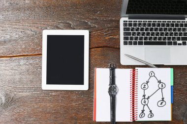 Dizüstü bilgisayar, tablet ve defter üzerinde ahşap bir masa vardır