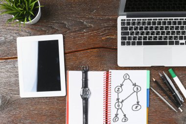 Dizüstü bilgisayar, tablet ve defter üzerinde ahşap bir masa vardır