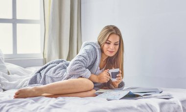 Mutlu genç kız yatakta seyahat için arama yapmak için telefon, tablet ve haritalar kullanarak