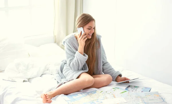 Šťastná dívka v posteli pomocí telefonu, tabletu a mapy k hledání cesty — Stock fotografie