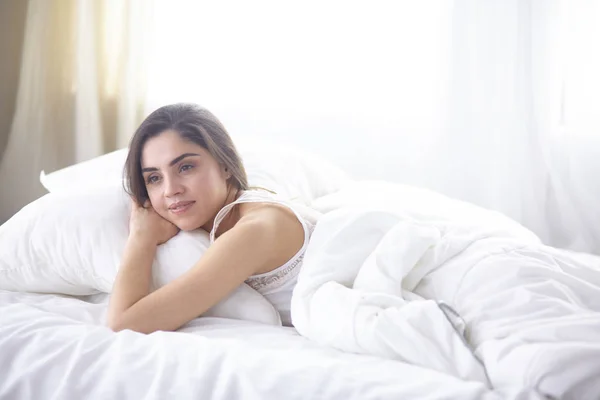 Krásná mladá žena ráno na výsluní v posteli. Krásný Model tvář vypadá sexy ve fotoaparátu — Stock fotografie