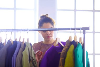 Pano raf giysi tasarımcısı ile yakınındaki beyaz arka plan üzerinde tutan güzel genç stilist