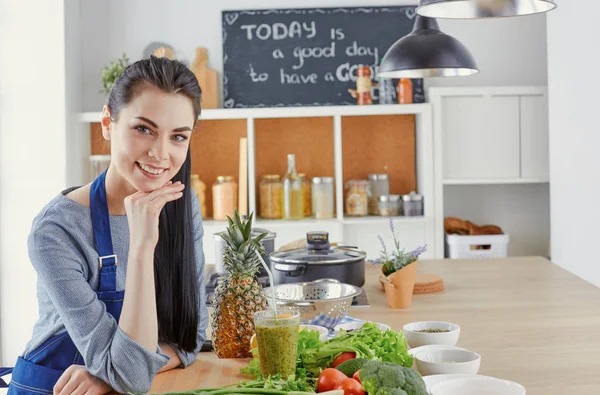 Glückliche junge Frau in der Küche mit frischem Gemüse auf dem Tisch — Stockfoto