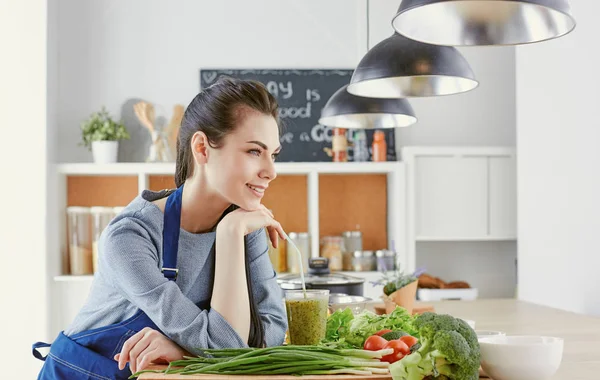 Happy young woman in kitchen with fresh vegetables on the table