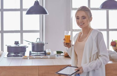 Mutfakta dijital tablet kullanan güzel genç bir kadın.