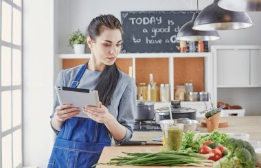 Mutlu kadın yemek tarifi arayan tablet mutfakta yemek yapıyor.