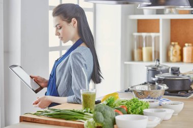 Mutlu kadın yemek tarifi arayan tablet mutfakta yemek yapıyor.