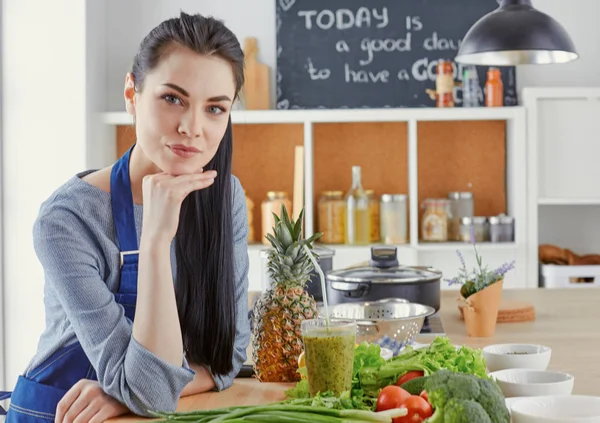 Glückliche junge Frau in der Küche mit frischem Gemüse auf dem Tisch — Stockfoto