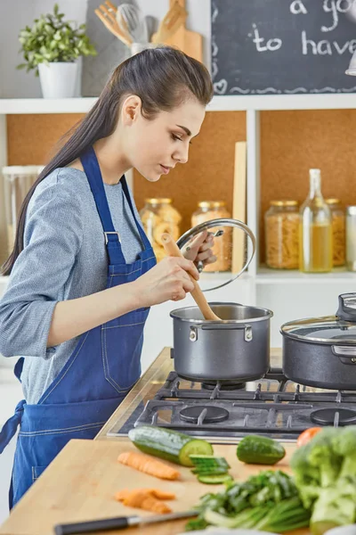 Bella ragazza sta assaggiando il cibo e sorridendo mentre cucina in kit — Foto Stock