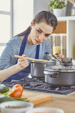 Güzel kız yemek tatma ve kit içinde pişirme sırasında gülümseyen