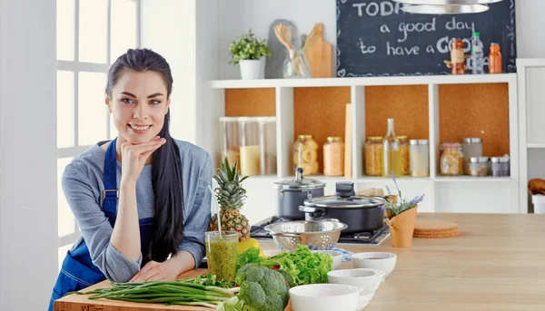 Happy young woman in kitchen with fresh vegetables on the table