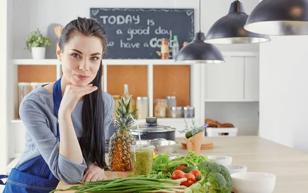 Glückliche junge Frau in der Küche mit frischem Gemüse auf dem Tisch — Stockfoto