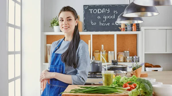 Happy young woman in kitchen with fresh vegetables on the table