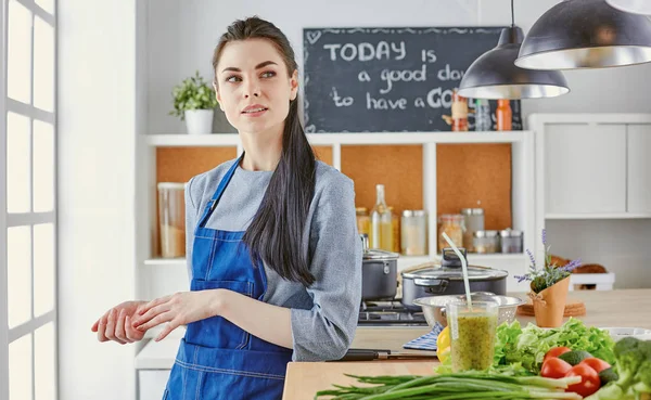 Ευτυχισμένος νεαρή γυναίκα στην κουζίνα με φρέσκα λαχανικά στο τραπέζι — Φωτογραφία Αρχείου