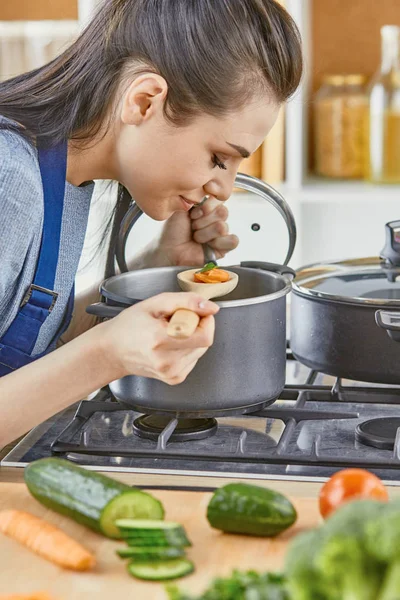 Bella ragazza sta assaggiando il cibo e sorridendo mentre cucina in kit — Foto Stock