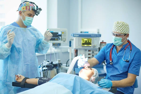 Vários médicos cercam o paciente na mesa de operação durante o trabalho. Cirurgiões de equipa a trabalhar na sala de operações — Fotografia de Stock