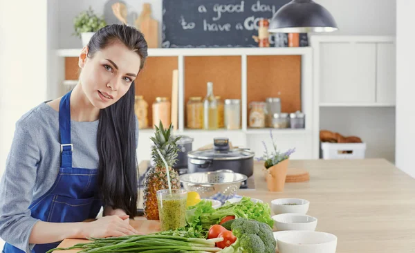 Glückliche junge Frau in der Küche mit frischem Gemüse auf dem Tisch — Stockfoto