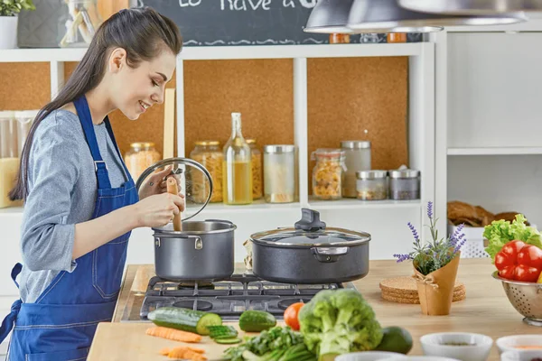 Beautiful girl is tasting food and smiling while cooking in kit — Stock Photo, Image