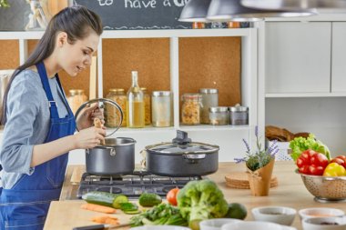 Güzel kız yemek tatma ve evde mutfakta yemek yaparken gülümseyen