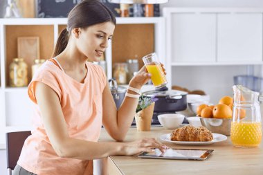 Cep telefonu görünümlü ve cam portakal suyu bir mutfakta Kahvaltı yaparken tutan gülümseyen güzel kadın