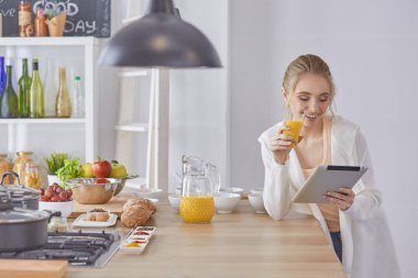 Mutfakta dijital tablet kullanan güzel genç bir kadın.
